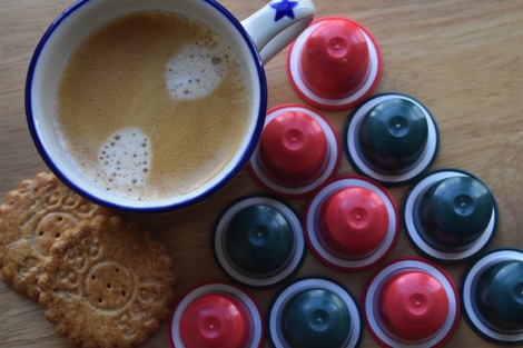 Small cup of coffee on a table with red and green Lost Sheep Coffee pods arranged in a triangle